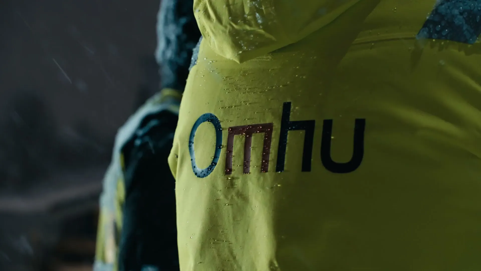 Rain falling on a yellow green jacket with the Omhu logo on the back