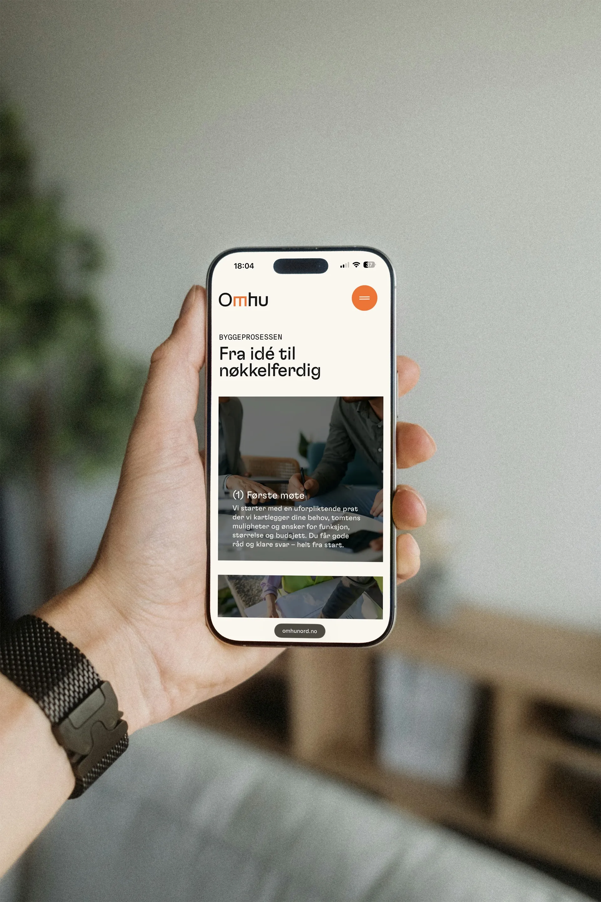 A hand holding a phone with Omhu’s website: “Fra idé til nøkkelferdig”