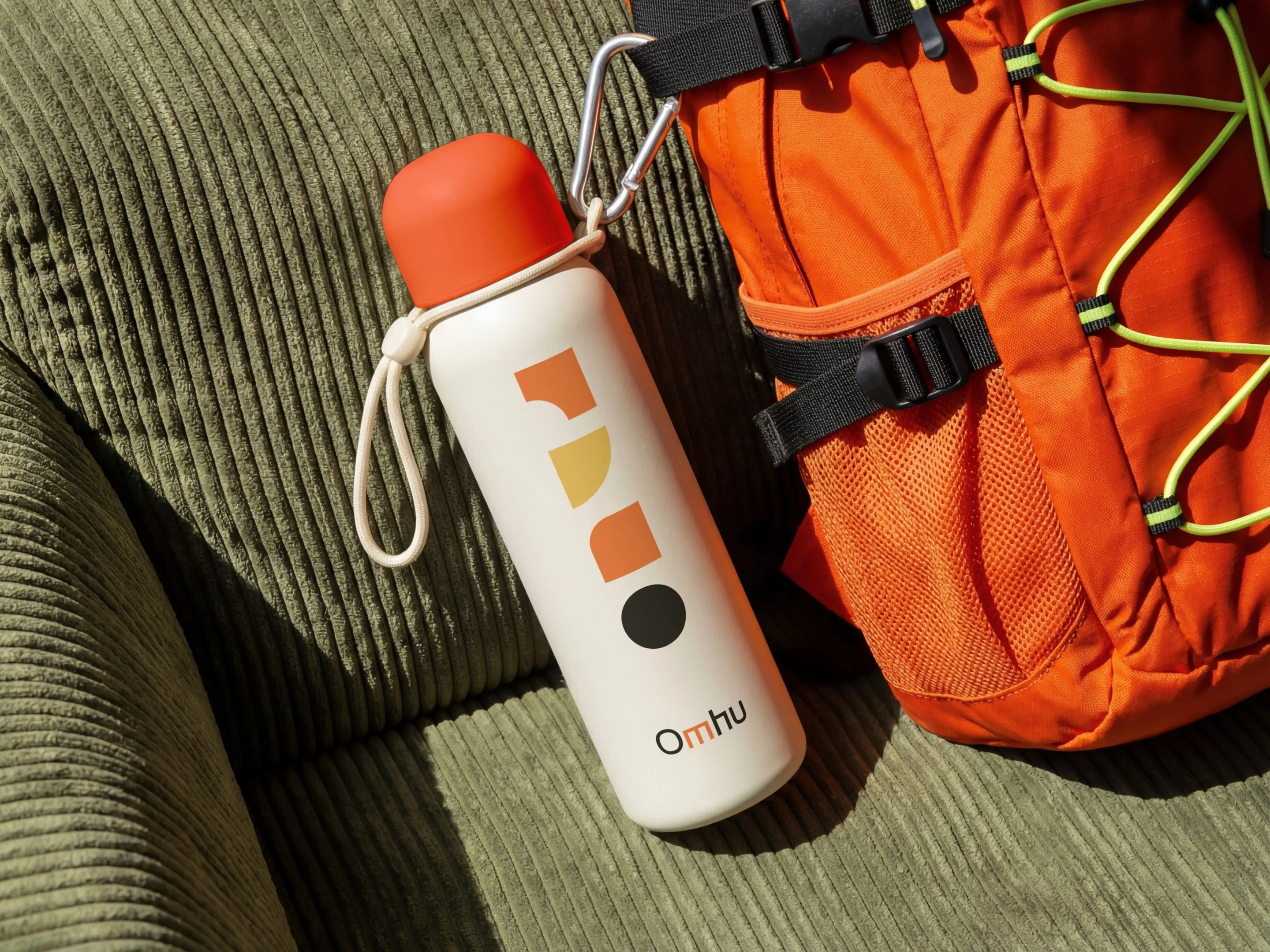 A water bottle with Omhu’s shapes next to an orange backpack