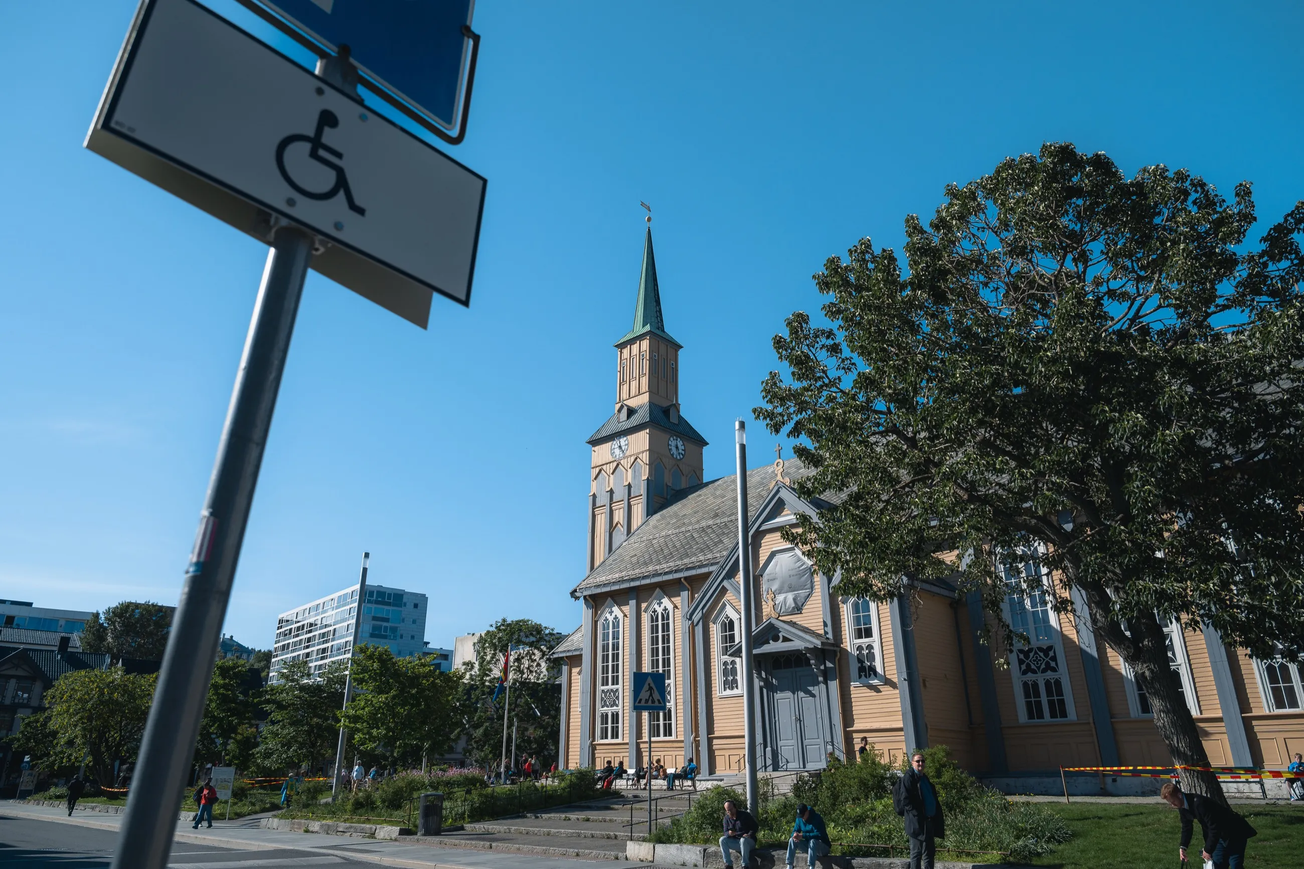 Tromsø domkirke, en gul trekirke med grønt spir, en solskinnsdag bak et parkeringsskilt
