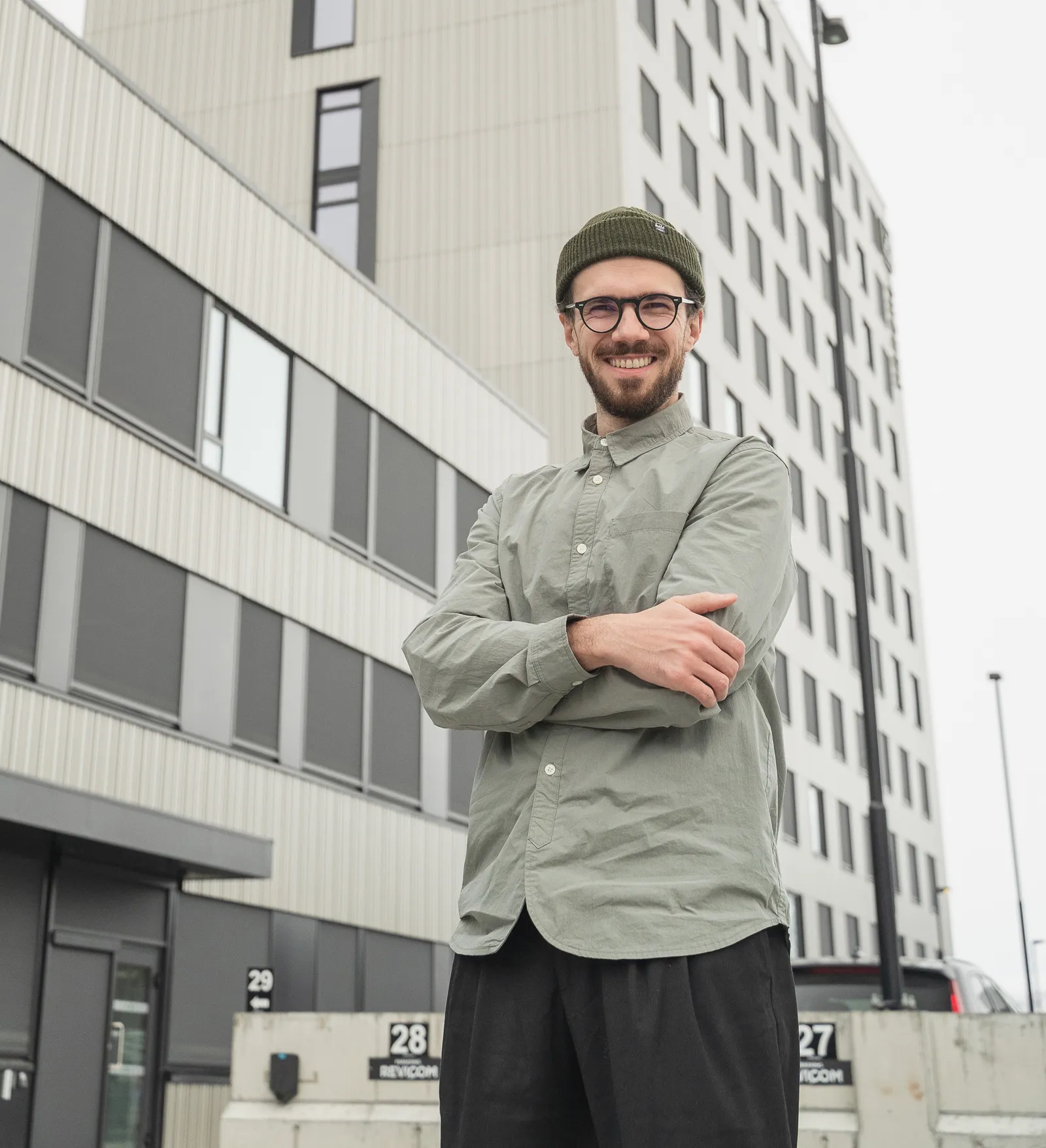 Radu smiler med armene i kors, foran grå kontorbygg