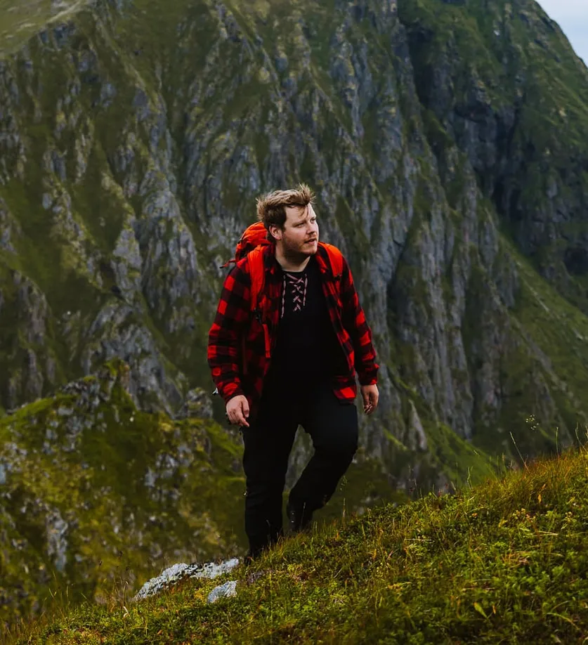 Vegard i rødrutete skjorte på vei opp en bratt, grønn fjellside